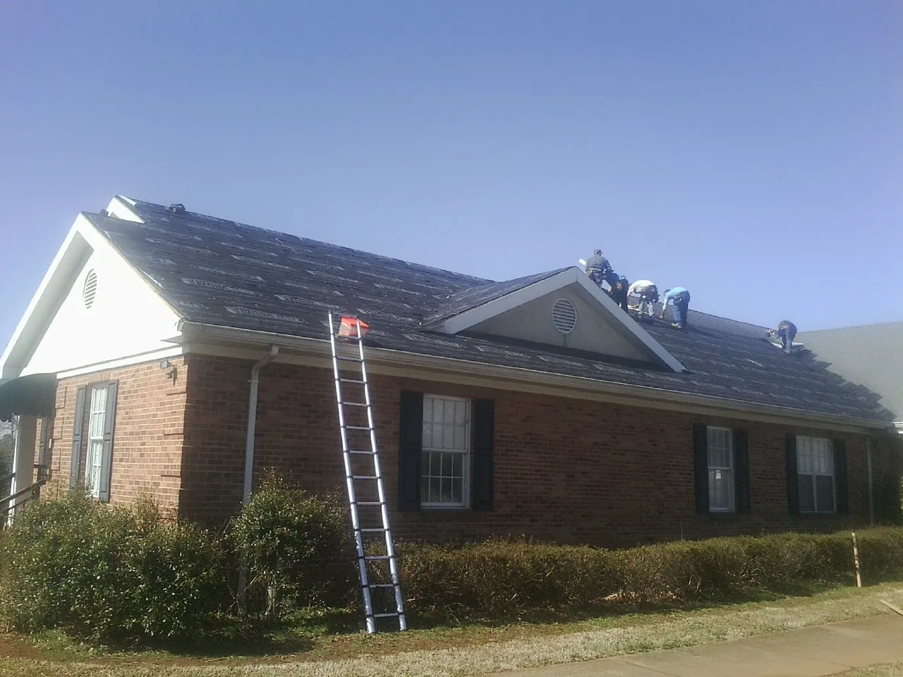 Crew tearing shingles off a brick ranch roof with a ladder set — Emergency Roof Repair work by our crew in Weyers Cave