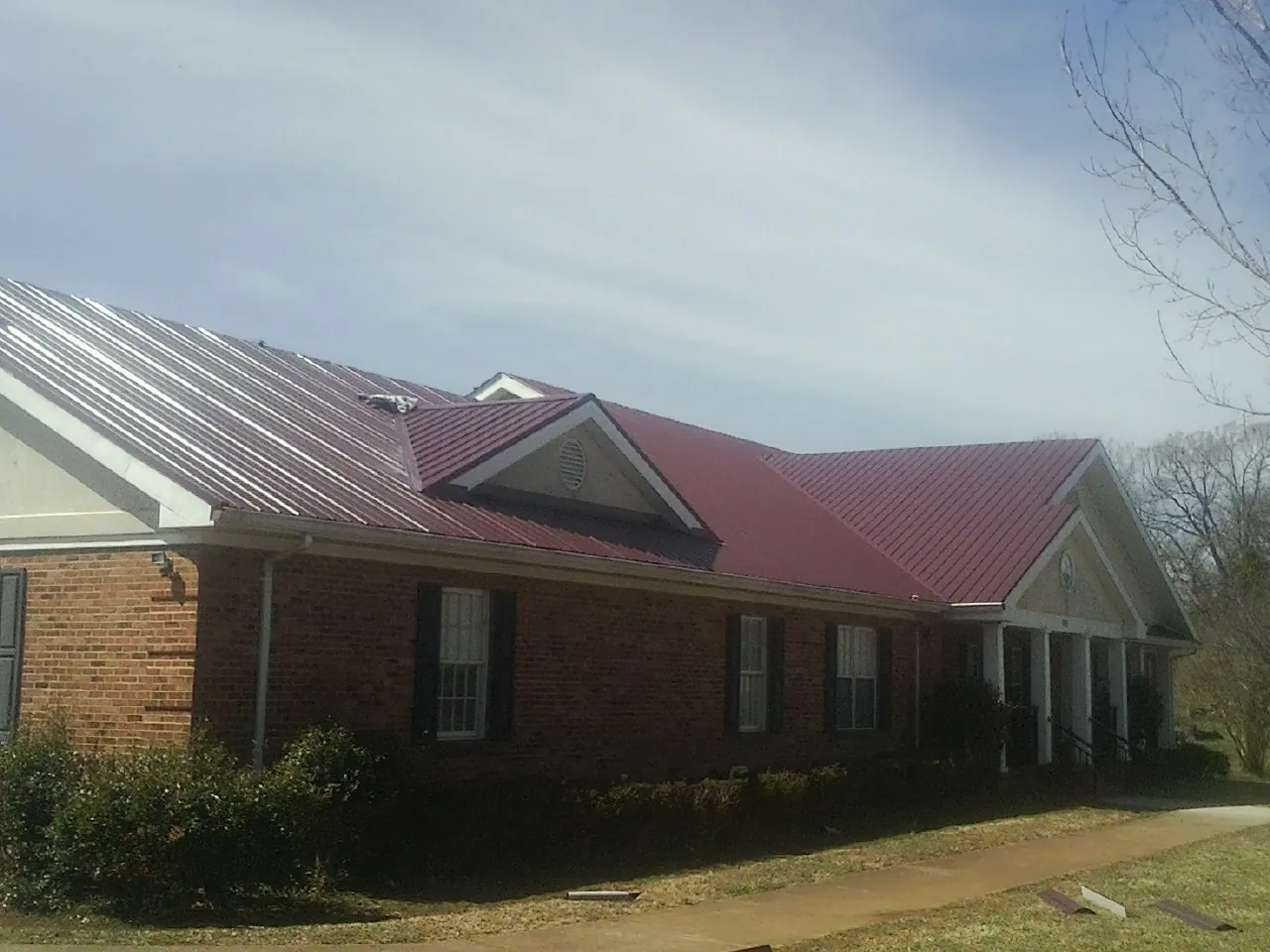 Red metal roof with gabled entries on a long brick building, from a Hail Damage Roof Repair job in Weyers Cave