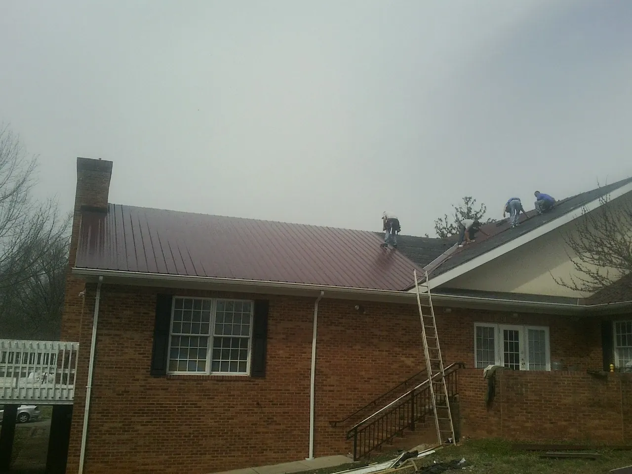 Crew setting red metal roofing panels on a brick home in Weyers Cave