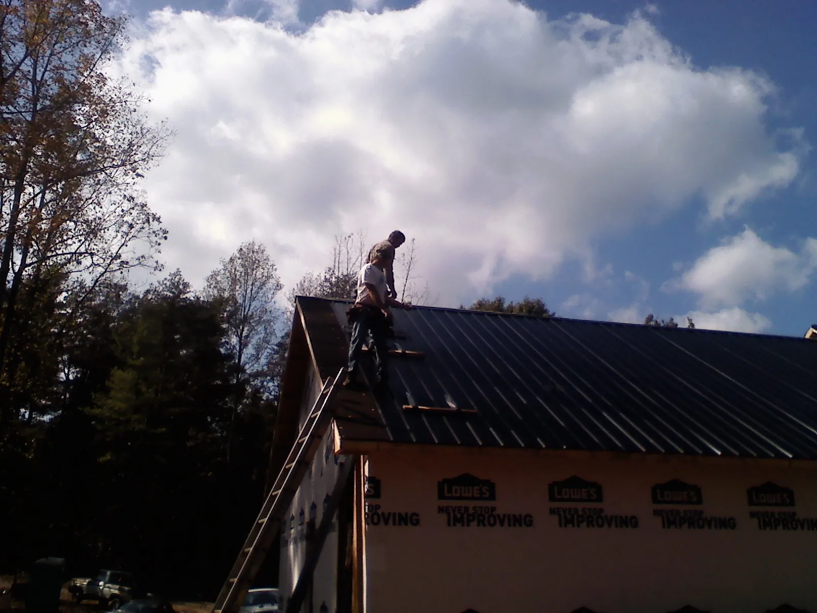 Roofer fastening dark metal panels high against a cloudy sky, from a Roof Inspection job in Weyers Cave