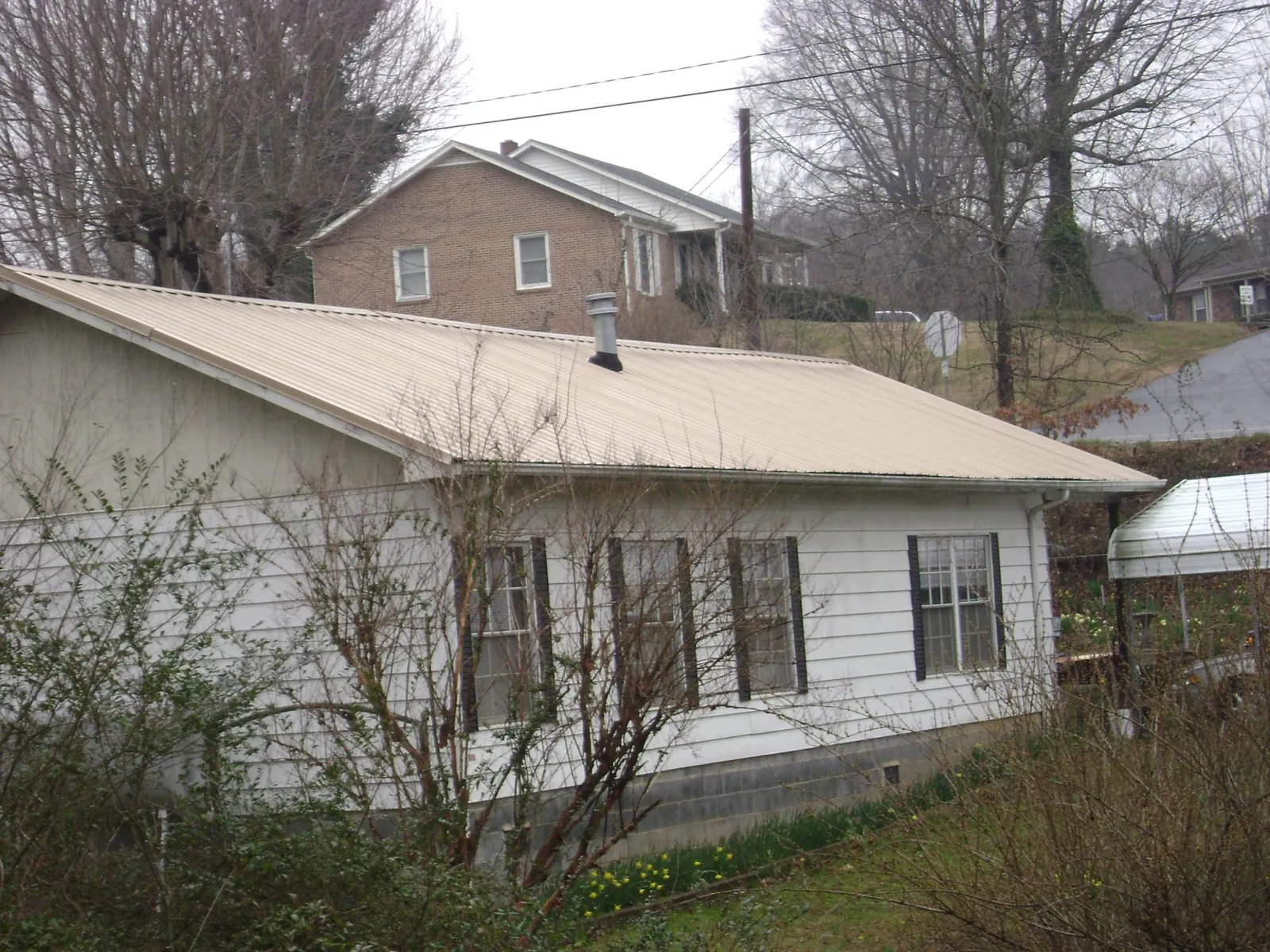 Tan metal roof on a white sided house set into a hillside — Commercial Roofing by Roofing Brothers in Weyers Cave